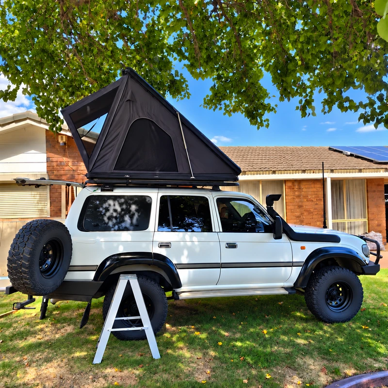 Black triangular rooftop tent mounted on a white off-road vehicle