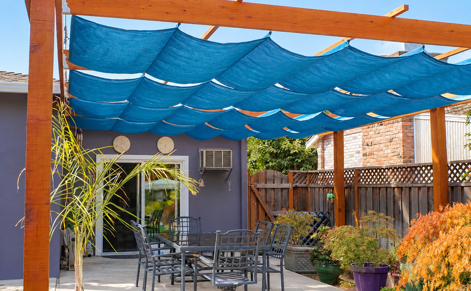Blue fabric wave panels suspended beneath a timber pergola above a patio seating area.