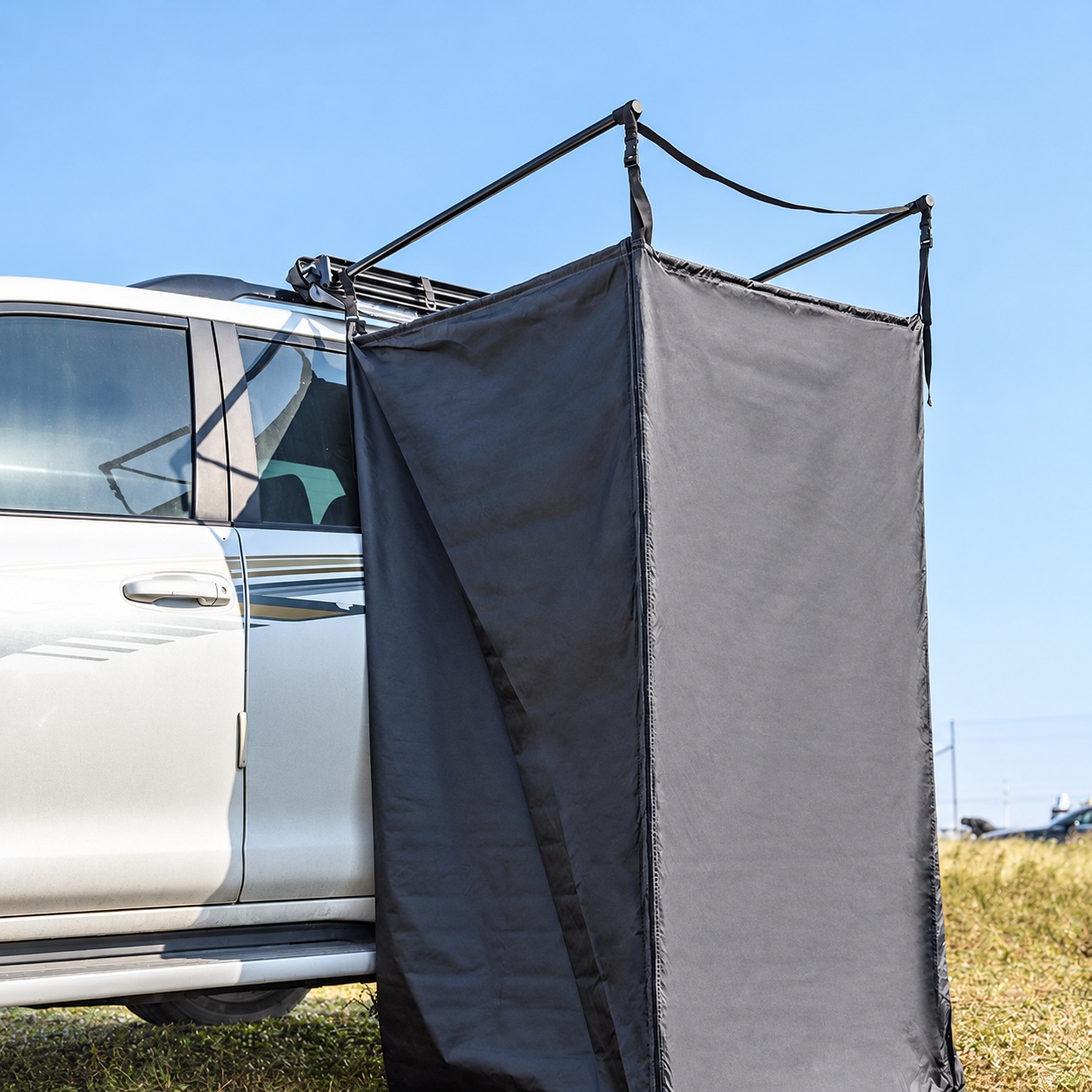 Grey open-top privacy enclosure beside a vehicle, suspended from extended black folding arms.