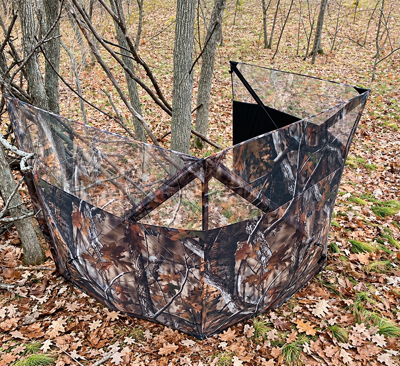 Camouflage observation screen with angled panels and exposed hub frames in a wooded setting.